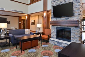 A hotel lobby with a stone fireplace, a flat-screen TV mounted on the wall, a sofa, a chair, and a coffee table.