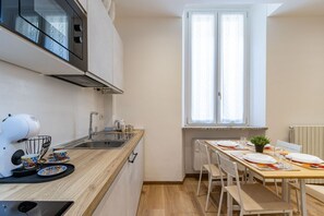 Eine kompakte Küche mit Mikrowelle, Wasserkocher und Kaffeemaschine, einem Spülbecken und einer Essecke mit Tisch für zwei Personen.