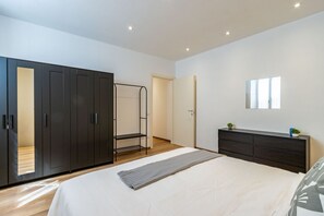 Een moderne slaapkamer met een groot bed, een kledingkast, een spiegel en een kleine plant op het nachtkastje.