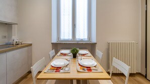 A dining area with a wooden table set for four, white chairs, a potted plant, and a window with curtains. - The Lane, Arona Center, AC, Wi-Fi by Guestaly (Arona)