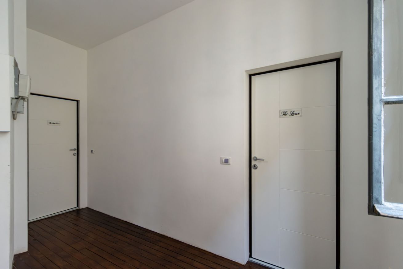 Ein Korridor mit zwei Türen, eine beschriftet mit 'The Lane', die andere mit einem Schild darüber. Der Boden ist aus Holz, und die Wände sind schlicht weiß.