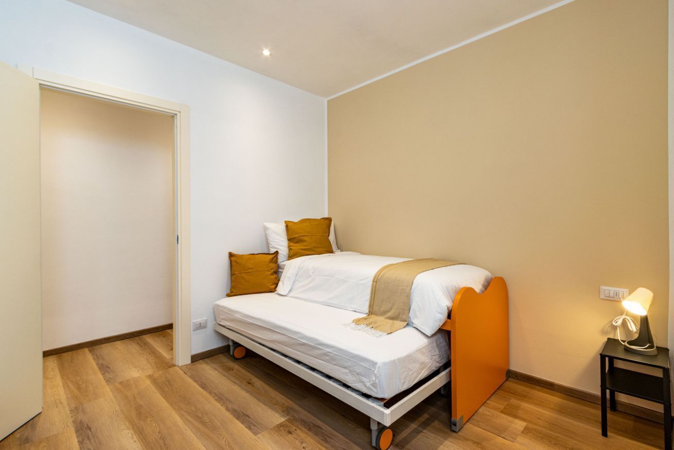 Un letto singolo con testiera, un comodino con una lampada e un pavimento in legno.