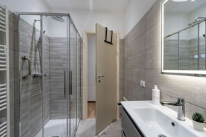 Een moderne badkamer met een glazen douchecabine, een witte wastafel met spiegel, en een beigekleurde deur.