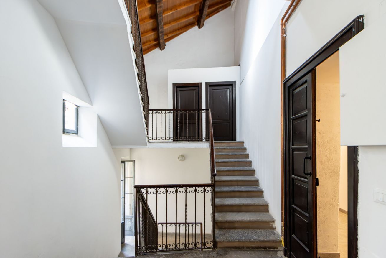 Eine Treppe mit Metallgeländer führt zu einer zweiten Etage, einer Tür und einem kleinen Fenster.
