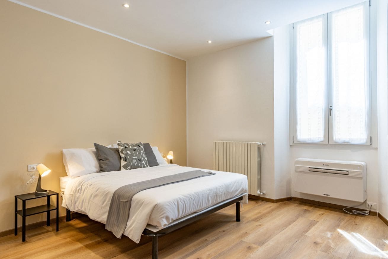 Ein Schlafzimmer mit einem Bett, Nachttischlampen, einem Heizkörper und einem Fenster.