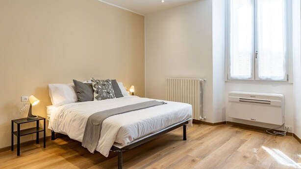 A bedroom with a bed, bedside lamps, a radiator, and a window. - The Lane, Arona Center, AC, Wi-Fi by Guestaly (Arona)