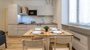 A modern kitchen with a dining area set for four, featuring a microwave, stove, and a window with curtains. - The Lane, Arona Center, AC, Wi-Fi by Guestaly (Arona)