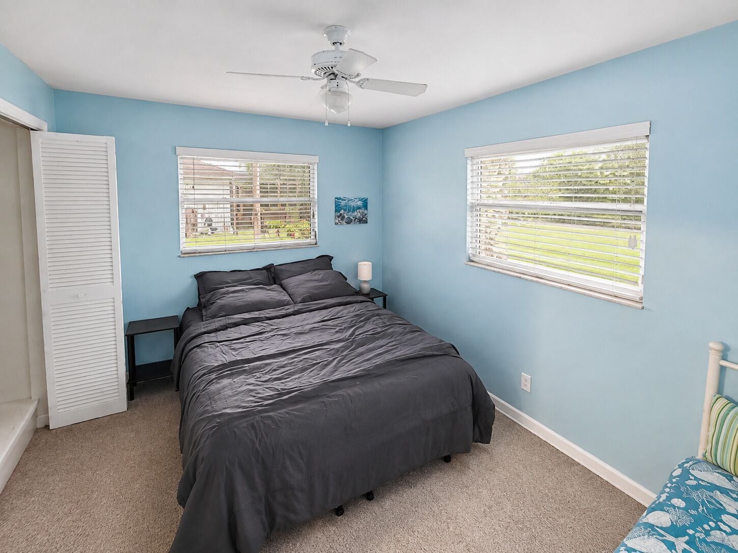 A bedroom with a bed, two windows with blinds, a ceiling fan, and a door.