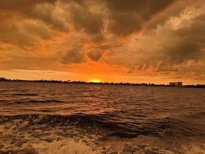 Ein Sonnenuntergang über einem Gewässer mit einer fernen Küstenlinie und Gebäuden.