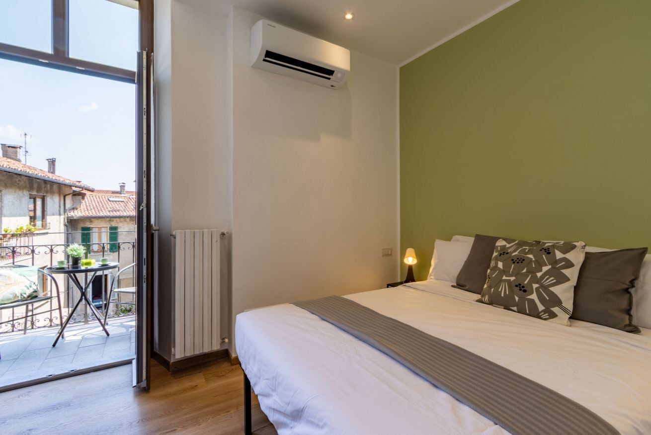 A hotel room with a bed, a radiator, an air conditioning unit, a table with chairs, and a view of the outside.