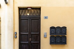 Eine dunkle Holztür mit einem Metallgitter, ein Briefkasten mit der Nummer 6 und zwei weitere an der Wand befestigte Briefkästen.