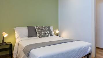 A neatly made bed with a white duvet and gray throw, two bedside lamps, and a green wall.