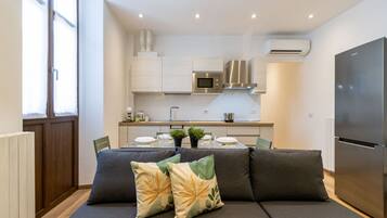 Eine moderne Küche mit weißen Schränken, einem Edelstahlkühlschrank und einem Essbereich mit einer Couch und Kissen.