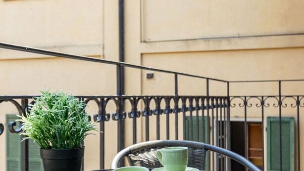 A balcony with a potted plant and a wicker chair with a table. - The Secret Court - Arona - AC - WiFi by Guestaly (Arona)