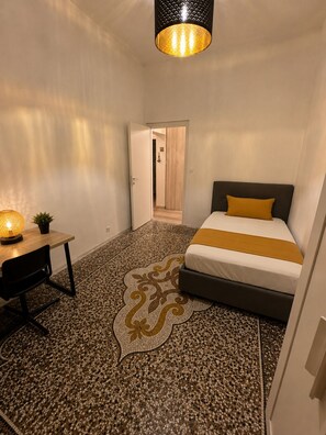 A bedroom with a bed, a desk, a chair, a patterned rug, and a door leading to another room. - Heart of Genoa, 5 min from Brignole (Genova)