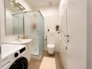 Ein modernes Badezimmer mit einer gläsernen Duschkabine, einem weißen Waschbecken, einer Toilette und einer Samsung Waschmaschine.