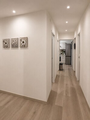 Ein Korridor mit Holzdielen, weißen Wänden und drei an der Wand befestigten Blumenbildern.