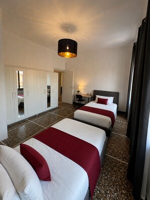 Ein Hotelzimmer mit zwei Betten, einem Schreibtisch, einem Stuhl, einem Kleiderschrank und einer Pendelleuchte.