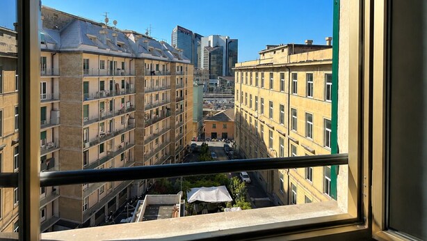Blick aus einem Fenster auf einen Stadtblick mit mehrstöckigen Gebäuden, darunter ein markanter Wolkenkratzer.