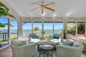 A spacious living room with a ceiling fan, large windows offering ocean views, and comfortable seating. - The Dream House / Gulf Front Luxury Retreat (Marathon)