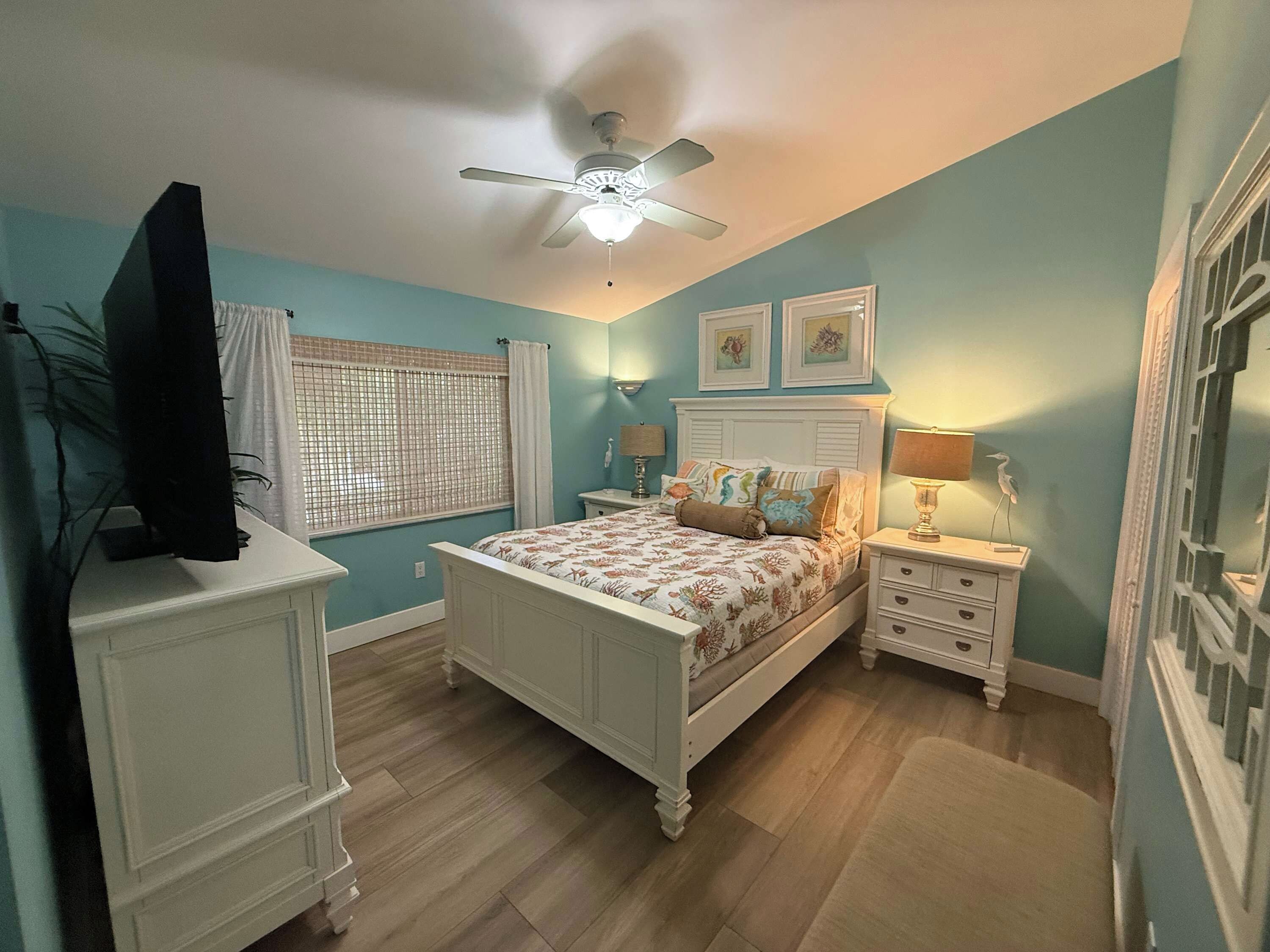 A bedroom with a bed, bedside tables, a ceiling fan, and a window with a curtain.