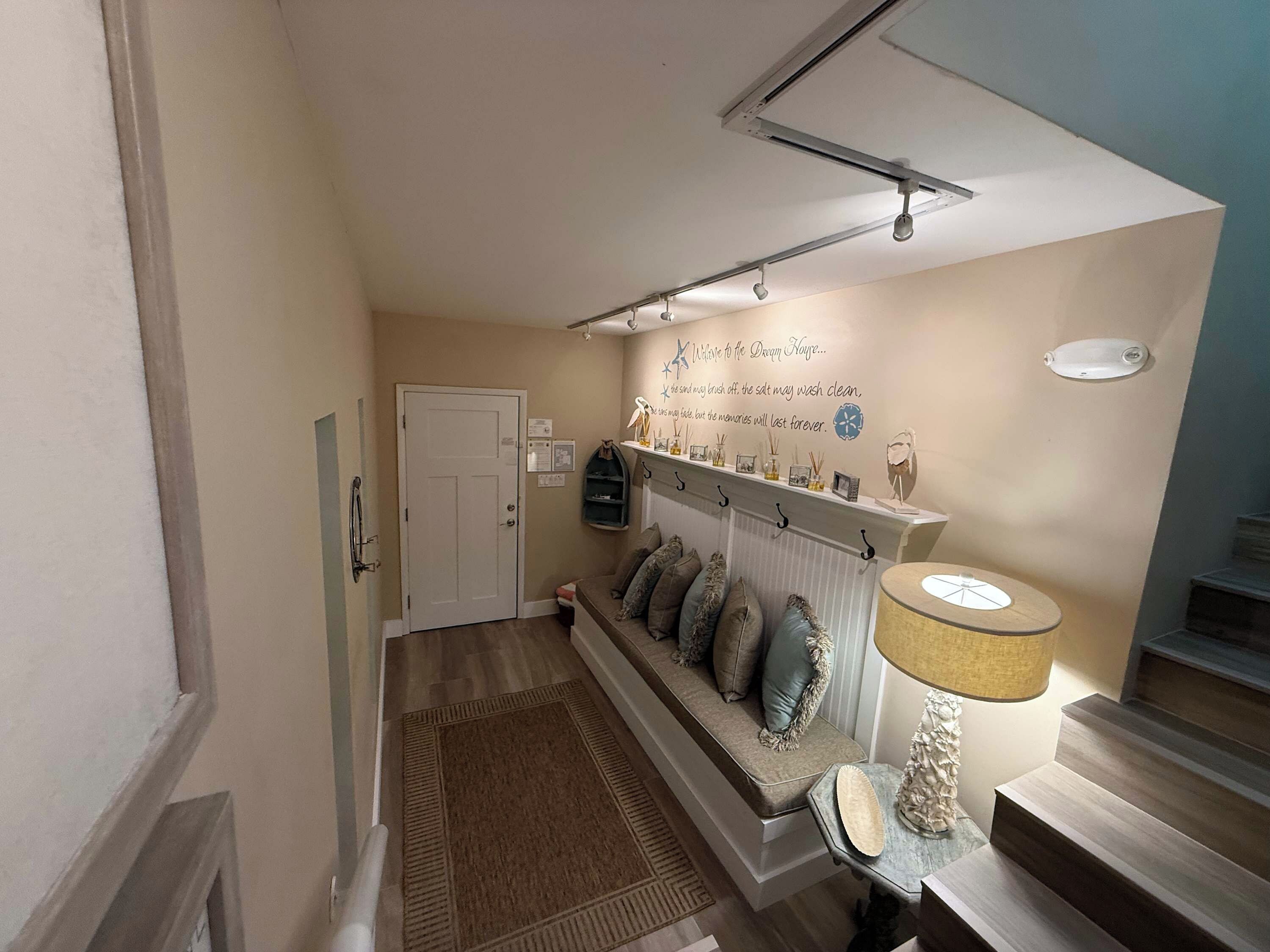 A hallway with a bench, a wall-mounted shelf with decorative items, a door, and a staircase.