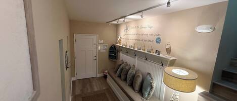 A hallway with a bench, a wall-mounted shelf with decorative items, a door, and a staircase.