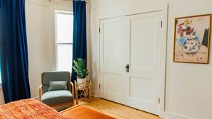 A bedroom with a bed, a chair, a potted plant, a door, and a painting on the wall. - Frida's House, Art-Filled Victorian in the Heart of Detroit (Detroit)