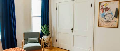 A bedroom with a bed, a chair, a potted plant, a door, and a painting on the wall.