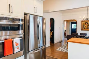 A modern kitchen with stainless steel appliances, a dining area with a wooden table, and a hallway leading to a living space. - Frida's House, Art-Filled Victorian in the Heart of Detroit (Detroit)