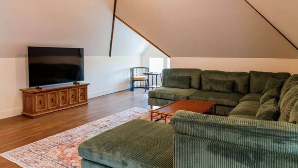 A modern loft apartment with a high ceiling, a large sectional sofa, a television on a wooden cabinet, and a small table. - Frida's House, Art-Filled Victorian in the Heart of Detroit (Detroit)