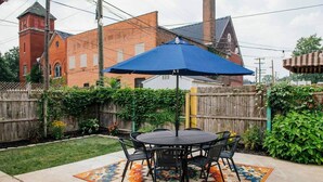 An outdoor patio with a round table and chairs, a blue umbrella, and a patterned rug. - Frida's House, Art-Filled Victorian in the Heart of Detroit (Detroit)