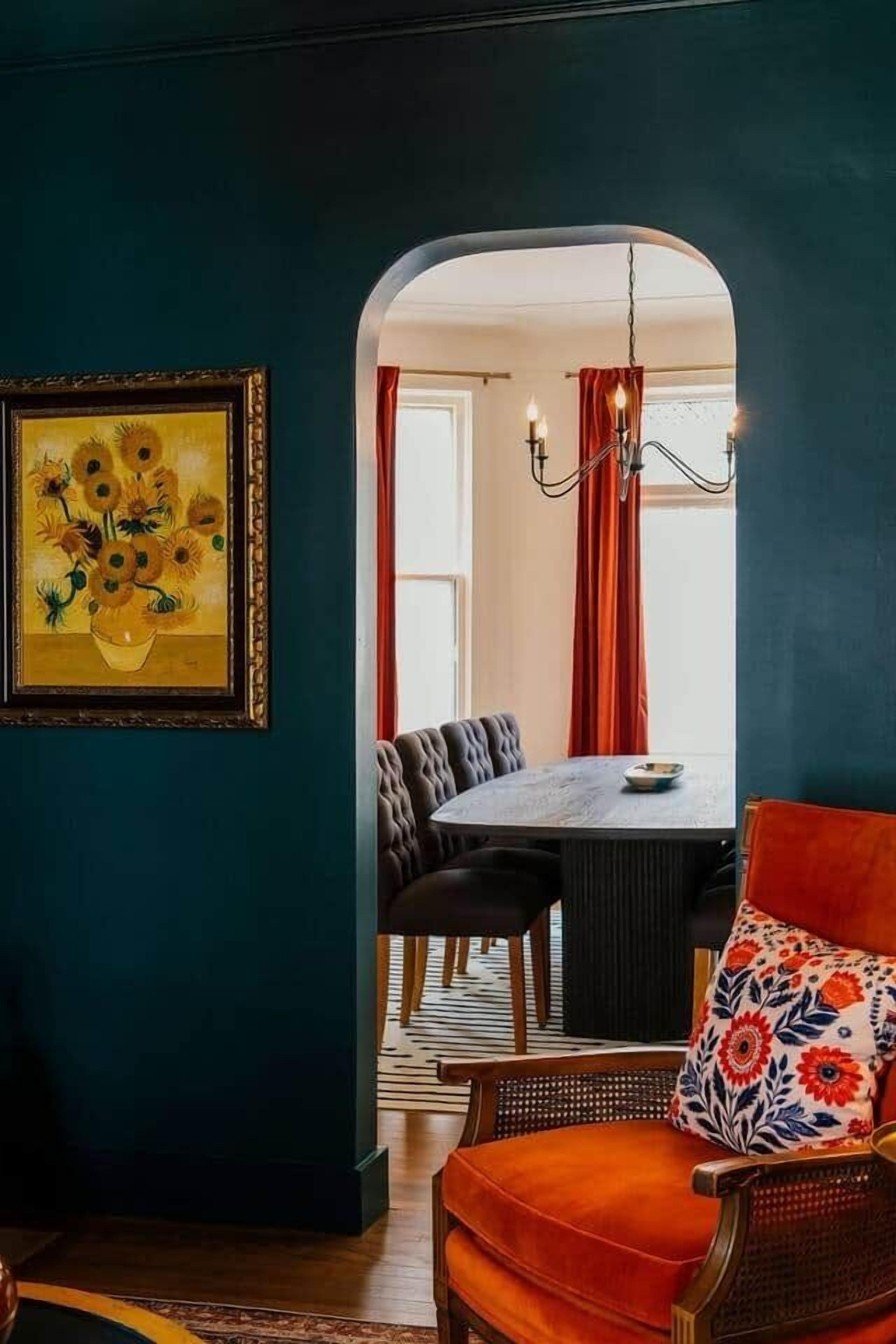 Een eethoek met een tafel en stoelen, een ingelijst schilderij aan de muur, en een zicht door een boog naar een andere kamer.