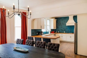 Eine moderne Küche mit weißen Schränken, einer turquoise farbenen Spritzschutzwand und einer zentralen Kochinsel. Es gibt einen Essbereich mit einem dunkelholztischen Tisch und gepolsterten Stühlen.