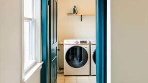 A laundry room with a front-loading washing machine and dryer, a window, and a shelf above the machines. - Frida's House, Art-Filled Victorian in the Heart of Detroit (Detroit)