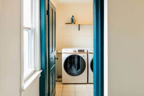 A laundry room with a front-loading washing machine and dryer, a window, and a shelf above the machines.