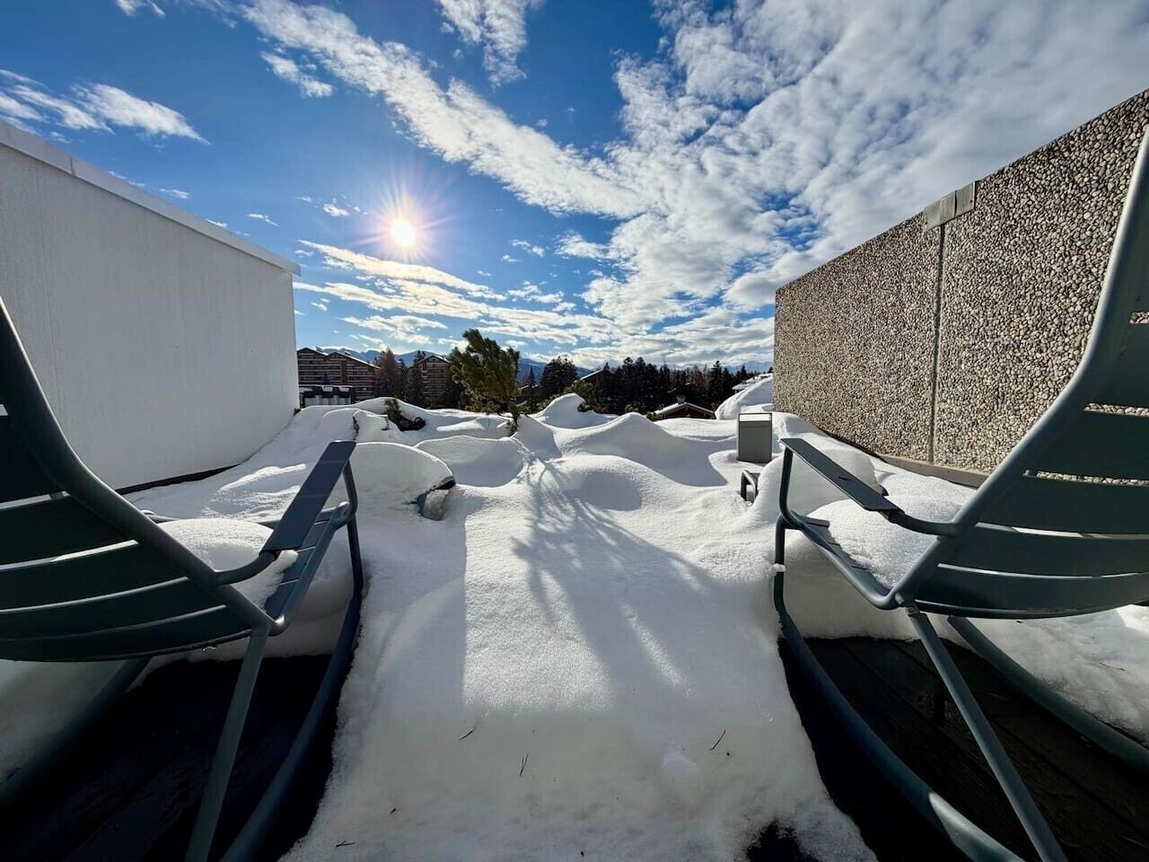 Un espace extérieur enneigé avec deux chaises en métal et un mur à la surface texturée.