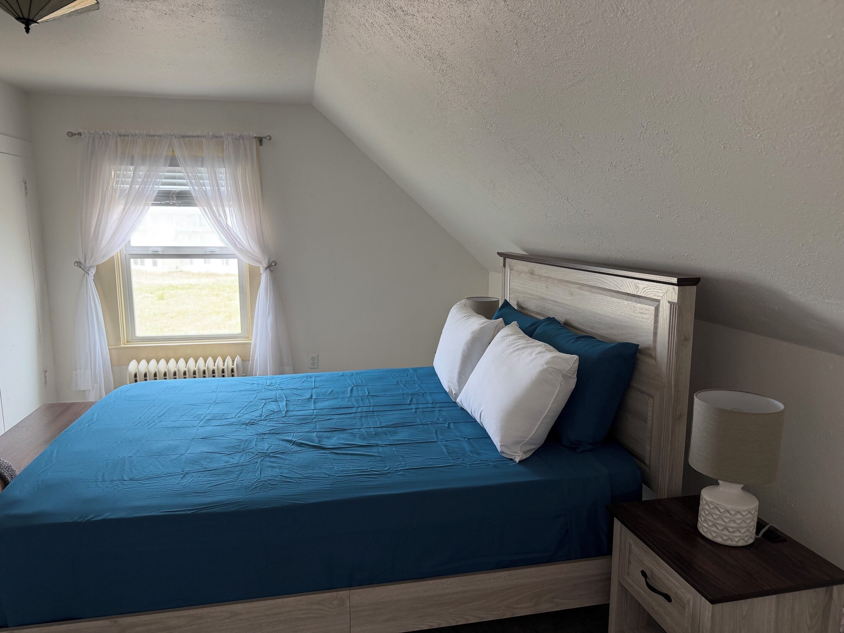 Une chambre à coucher avec un lit, une table de chevet, une lampe et une fenêtre avec des rideaux.