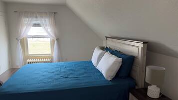 Une chambre à coucher avec un lit, une table de chevet, une lampe et une fenêtre avec des rideaux.