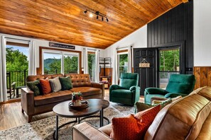 A spacious living room with a wooden ceiling, large windows, and a view of greenery. - NEW Dolly Fireworks View! 3 King, LuxHotTub, Fence Yd (Pigeon Forge)