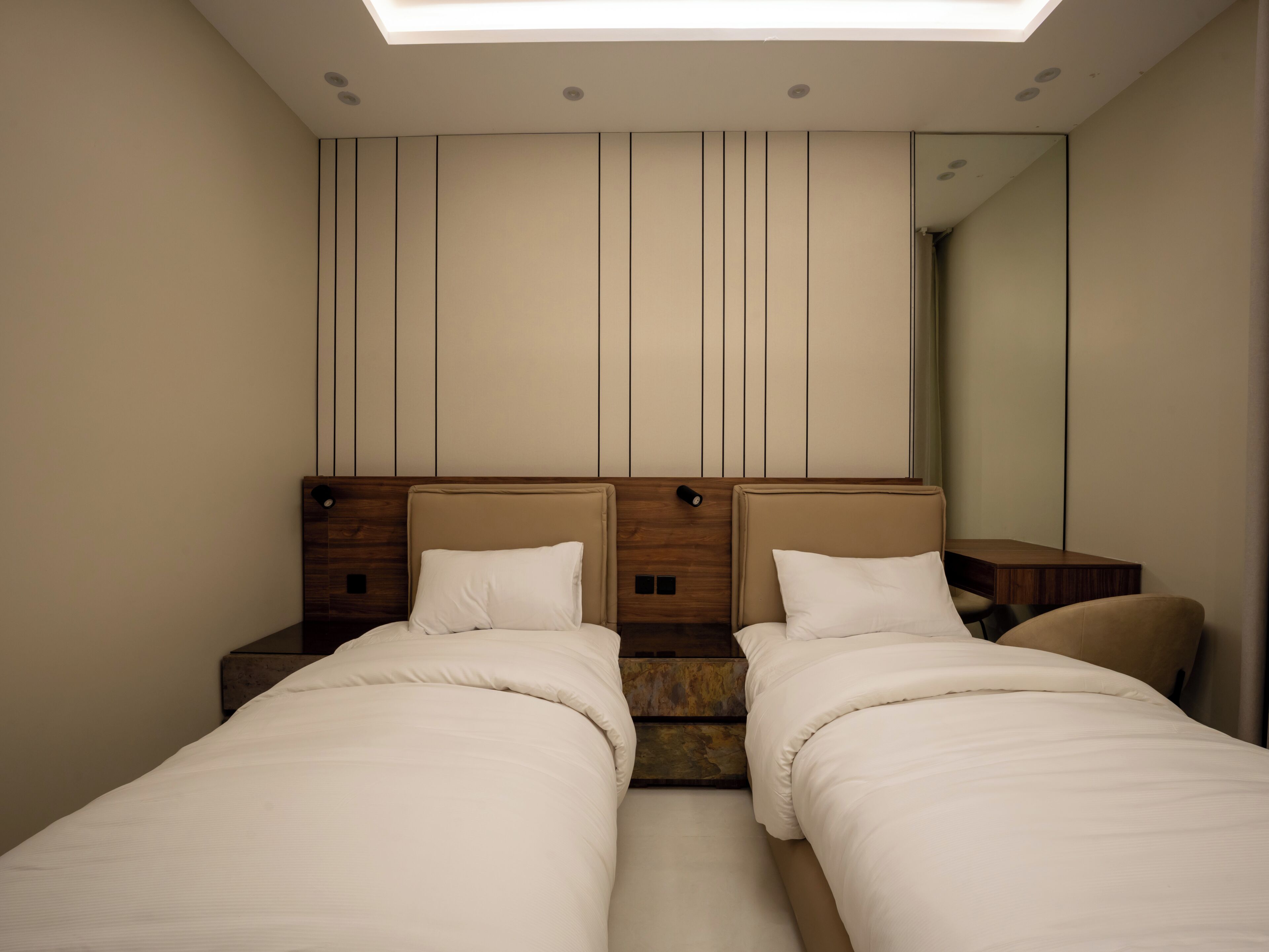 A hotel room with two beds, a wooden headboard, a mirror, and a skylight.