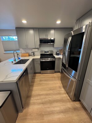 A modern kitchen with stainless steel appliances, grey cabinetry, and a wooden floor. - Cozy 2-bedroom house in Shoreline perfect for relaxing stays (Shoreline)