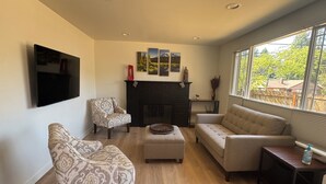A living room with a fireplace, a television mounted on the wall, and a large window offering a view of the outdoors. - Cozy 2-bedroom house in Shoreline perfect for relaxing stays (Shoreline)