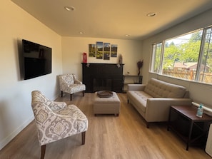 A living room with a fireplace, a television mounted on the wall, and a large window offering a view of the outdoors. - Cozy 2-bedroom house in Shoreline perfect for relaxing stays (Shoreline)