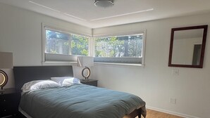 A bedroom with a bed, a nightstand, a mirror, and a window with a view of trees. - Cozy 2-bedroom house in Shoreline perfect for relaxing stays (Shoreline)