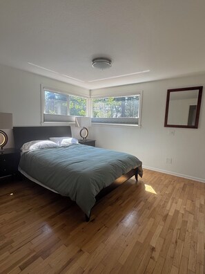 A bedroom with a bed, a nightstand, a mirror, and a window with a view of trees. - Cozy 2-bedroom house in Shoreline perfect for relaxing stays (Shoreline)