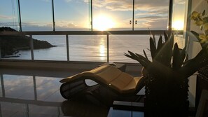 Sillón de descanso con vista al océano y al atardecer a través de amplias ventanas.