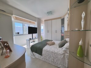 Un dormitorio moderno con cama, televisor, armario y escritorio.