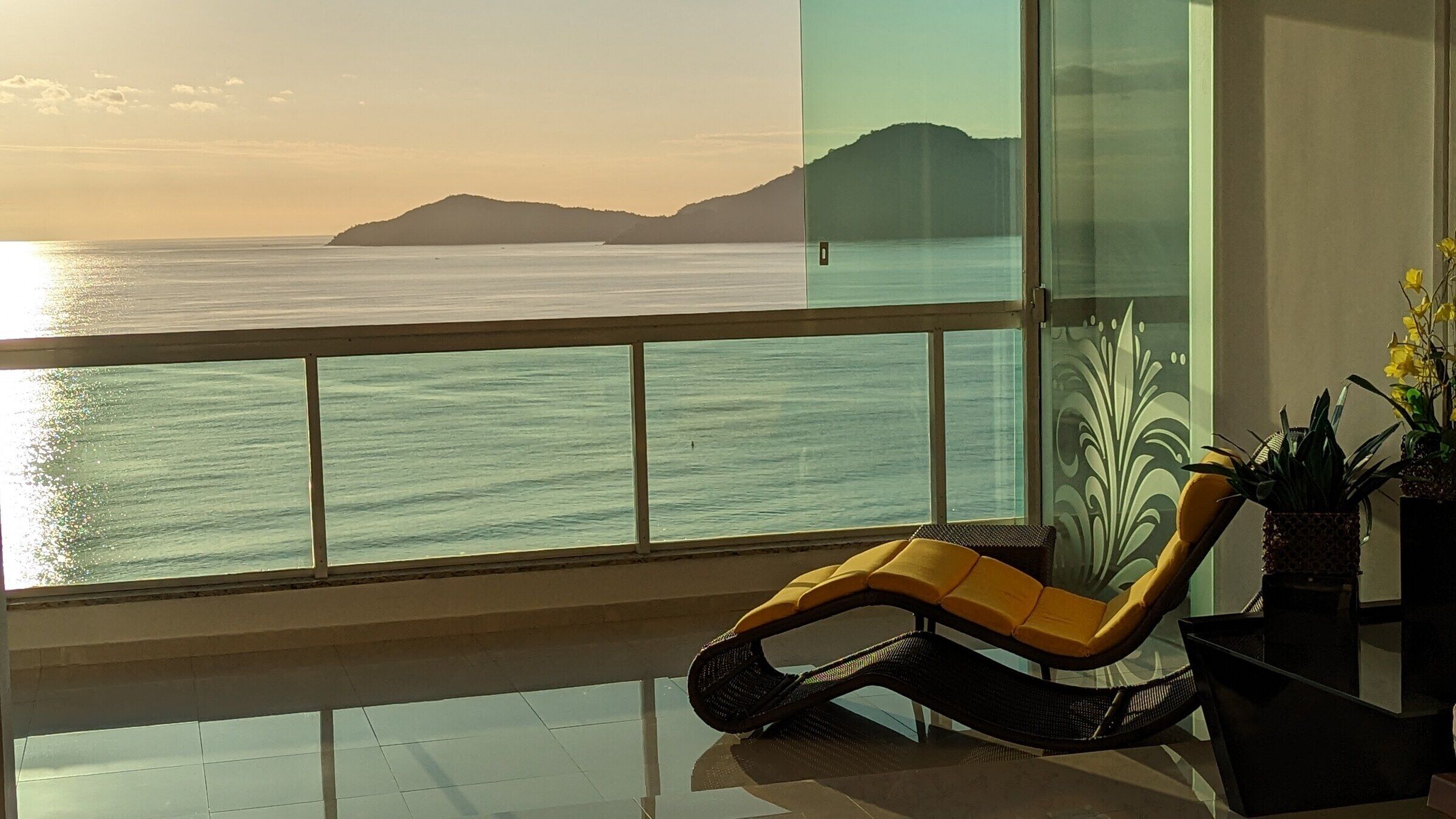 A balcony with a view of the sea and a chair.