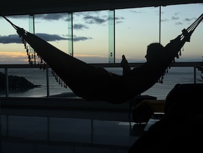 A person relaxing in a hammock by a window overlooking a body of water.